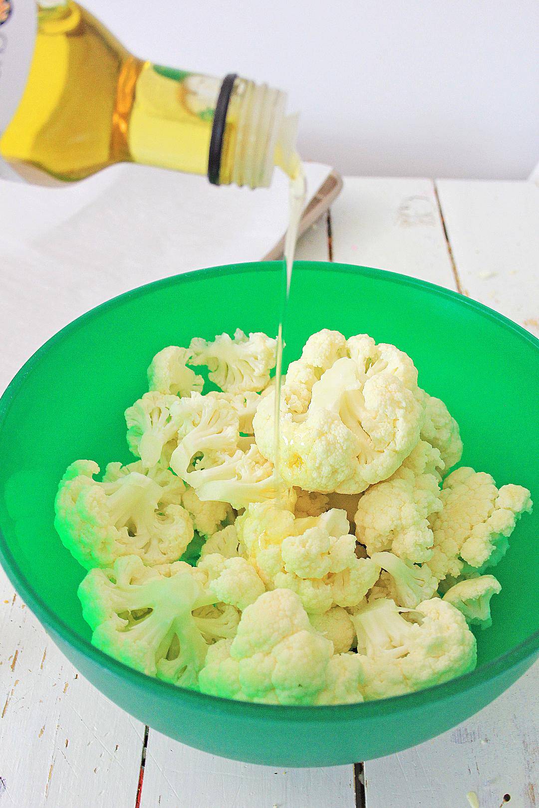 Olive oil being drizzled on top of cauliflower in green bowl.