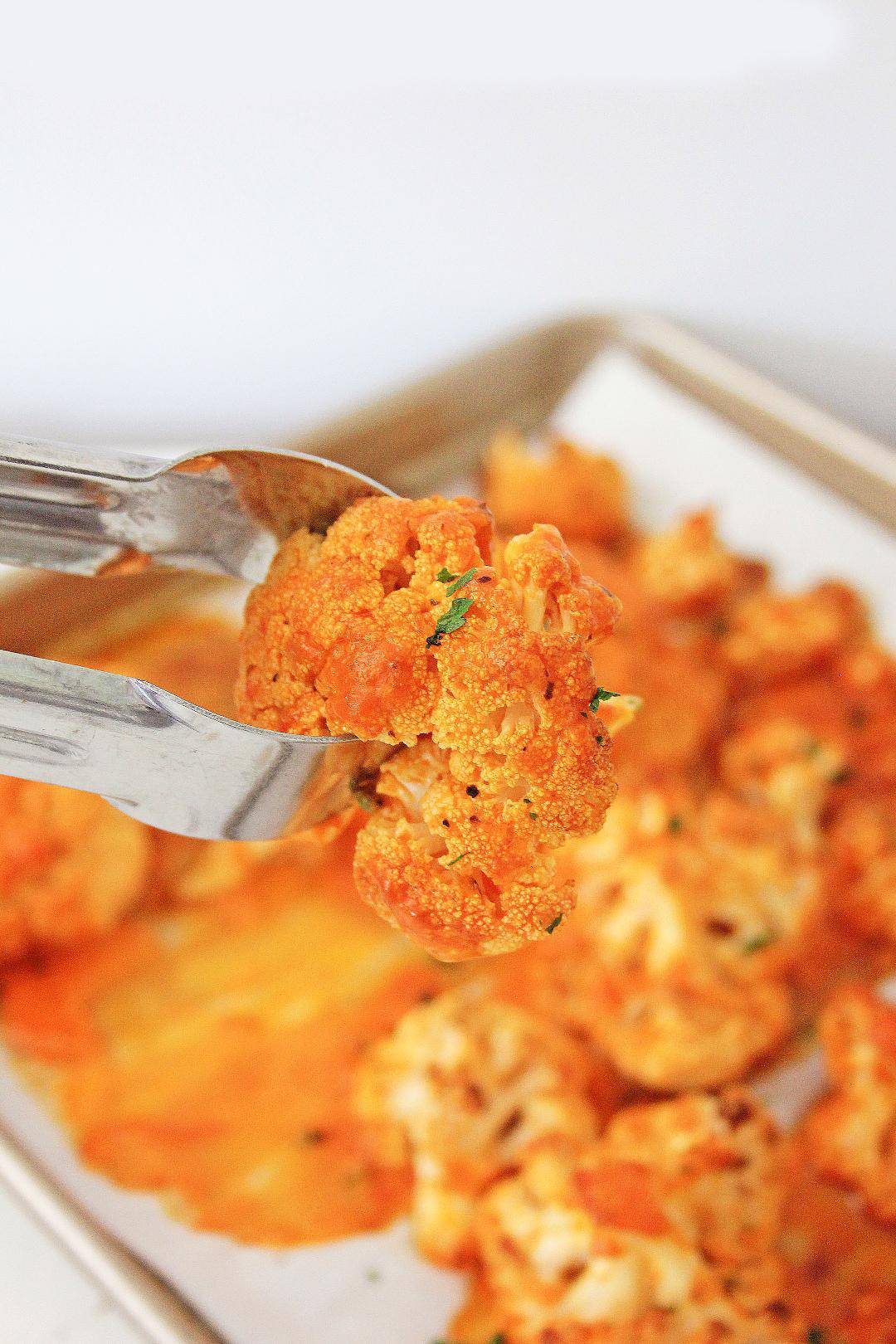 Closed up of tongs holding roasted buffalo cauliflower.