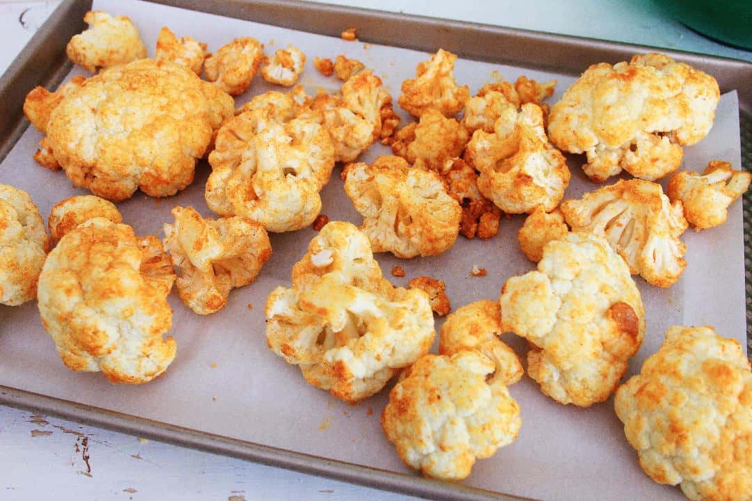 Seasoned cauliflower on sheet pan lined with parchment paper.