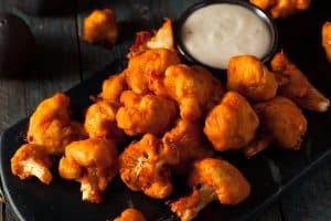 Roasted buffalo cauliflower on a black plate with blue cheese dressing.