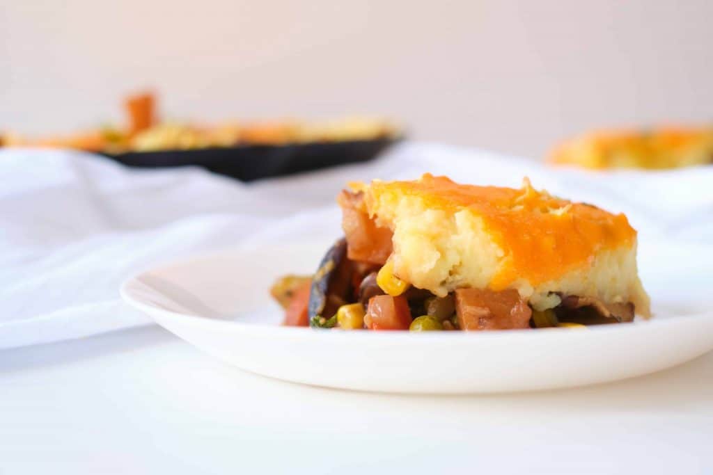 Head on photo of a piece of shepherd's pie on a white plate with a black iron skillet of it in the background.