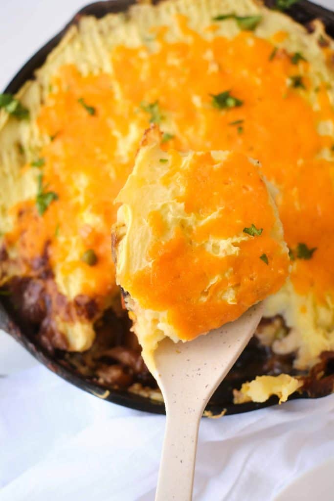 Shepherds Pie hot out of the oven with a spoonful of it on a wooden spoon.