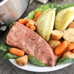 Corned beef with cabbage wedges, baby carrots and red potatoes on a bed of green cabbage on a white plate.