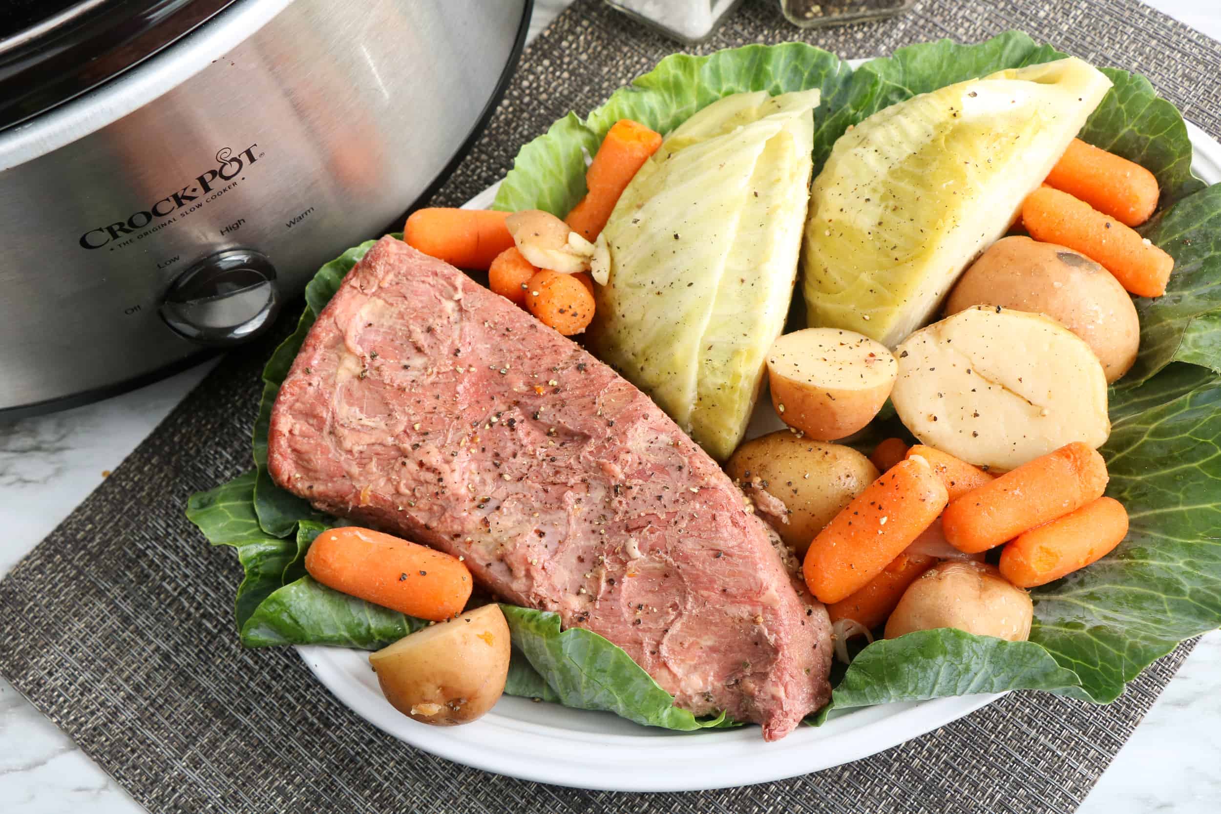 Corned beef with cabbage wedges, baby carrots and red potatoes on a bed of green cabbage on a white plate.