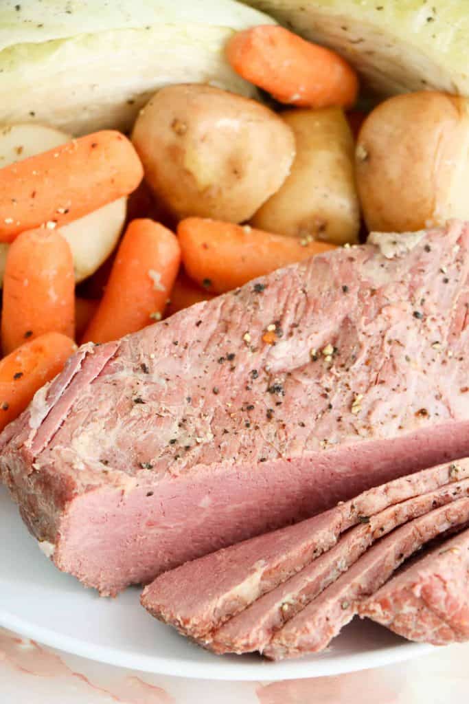 slow cooker corned beef on a white platter with cabbage, potatoes and carrots.