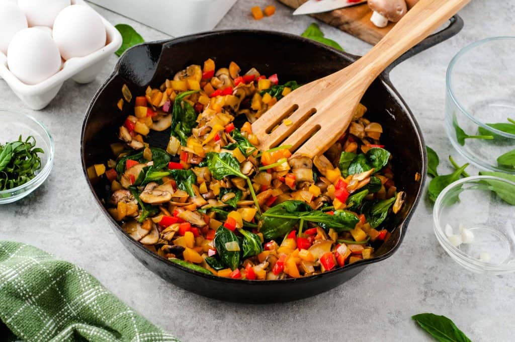 Bell peppers, spinach, mushrooms and onions sautéed in a black iron skililet.