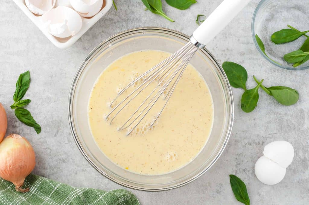 Eggs and milk whisked in a glass bowl.