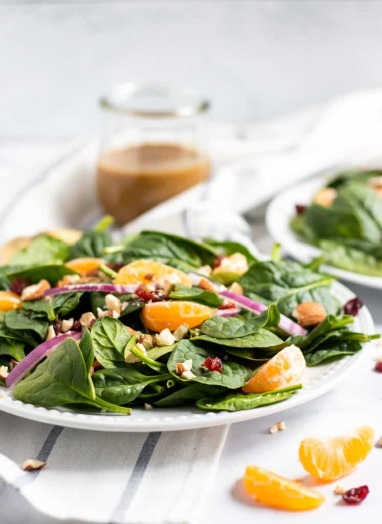 Spinach mandarin salad with honey balsamic background on white plate.