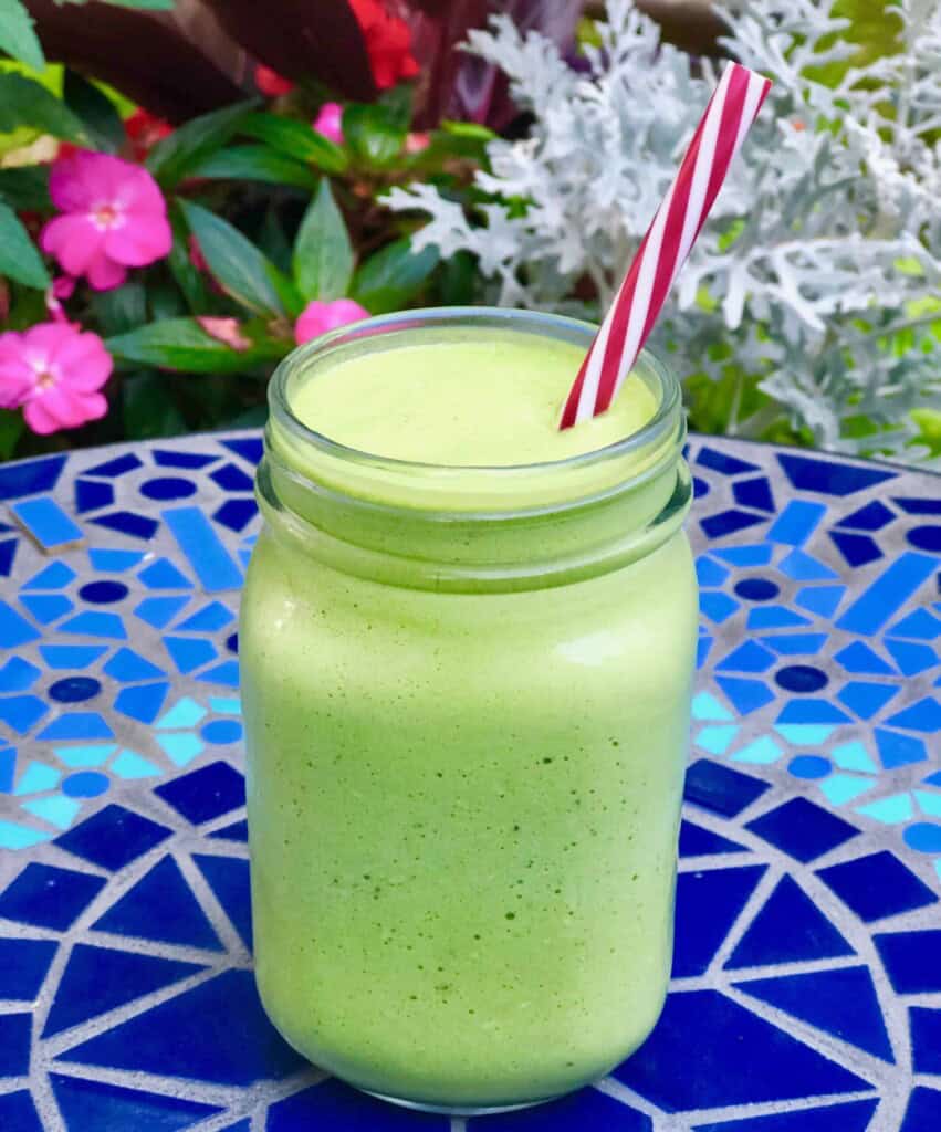 Tropical green smoothie on a blue tile background.