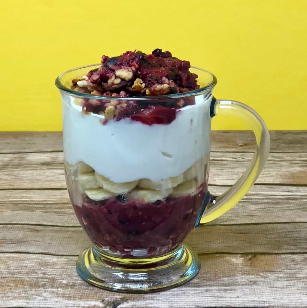 Berry granola parfait layered with fruit, bananas and vanilla greek yogurt with a wood background.