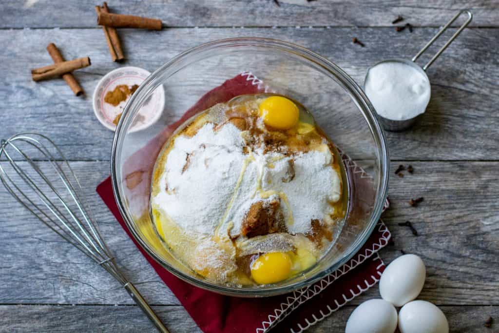 Pumpkin cheesecake bite ingredients in a bowl with cinnamon sticks, eggs and whisk on wood table