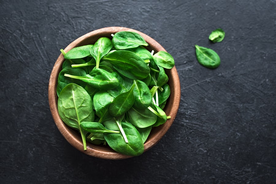 Baby spinach leaves in bowl on black background, top view, copy space. Clean eating, detox, diet food ingredient - green organic spinach.