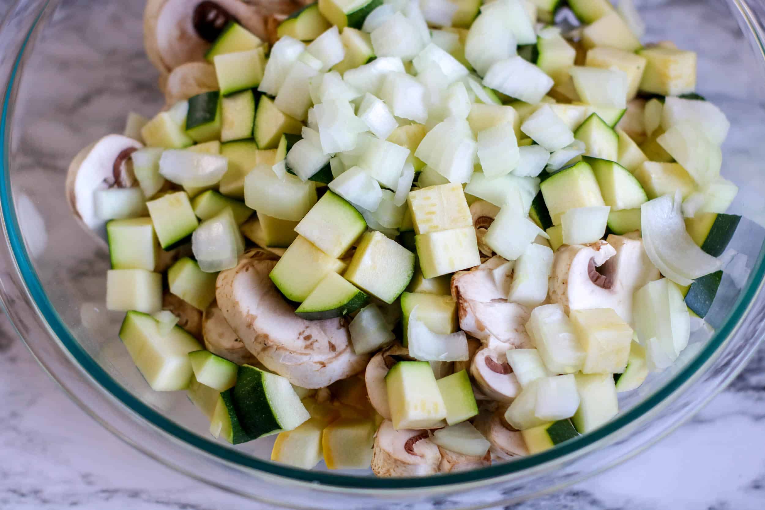 Chopped zucchini, squash, onion and mushrooms in a bowl.