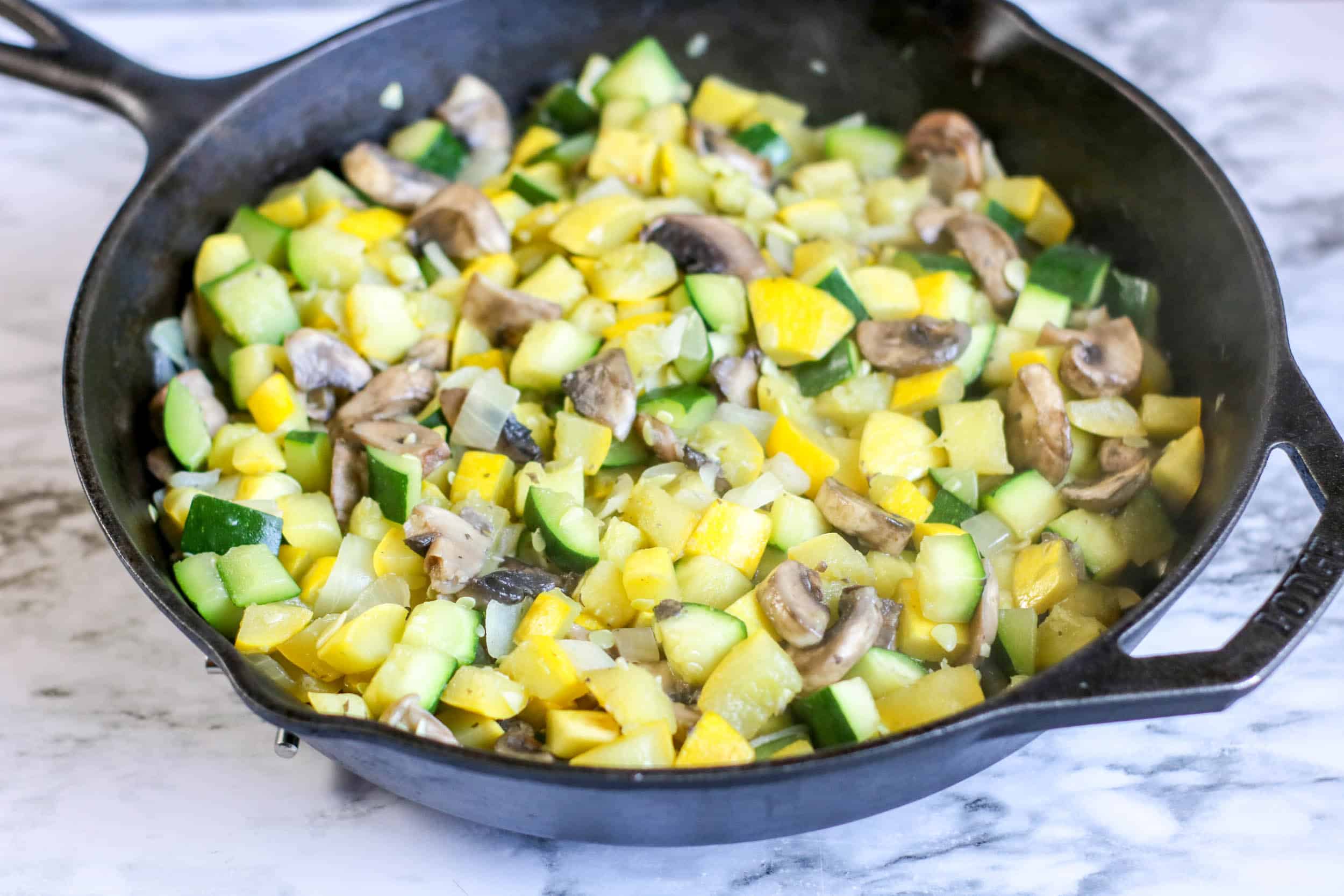 Chopped zucchini, squash, onion and mushrooms in a cast iron skillet.