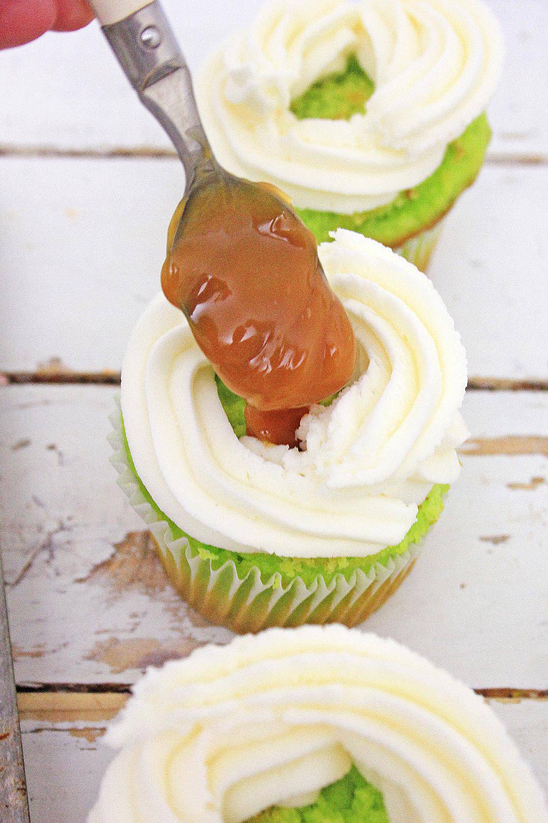 Caramel being placed in center of buttercream frosting in cupcake