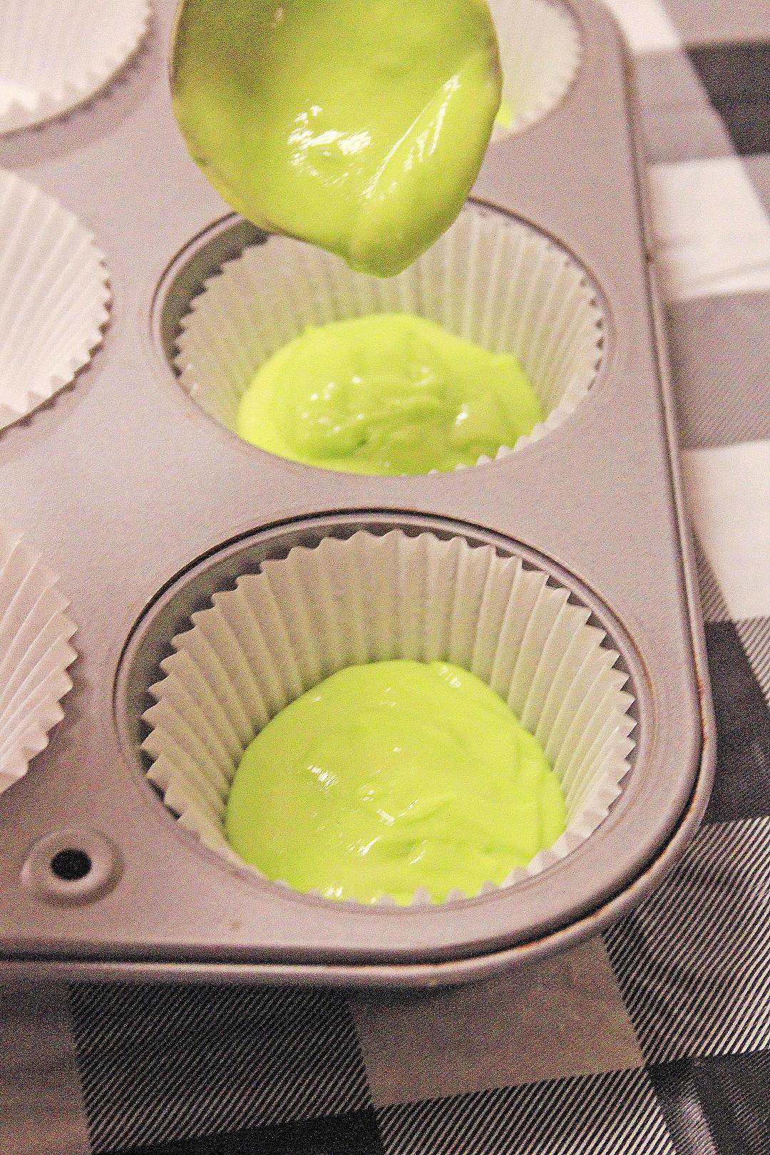Green cupcake batter being poured into muffin tin