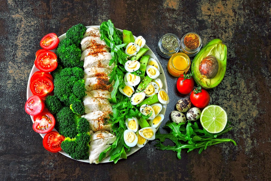Plate with a keto diet food. A set of products for the ketogenic diet on a plate. Cherry tomatoes, boiled broccoli, steamed chicken breast, salad with arugula, avocado and quail eggs. Keto lunch.