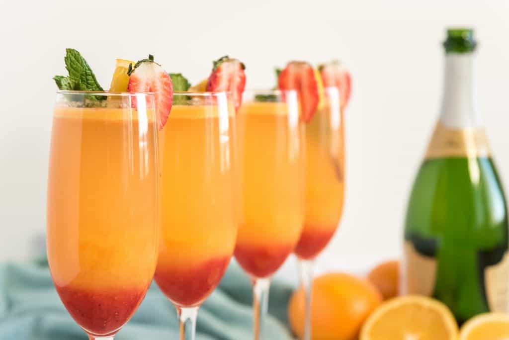 4 strawberry mimosas in champagne flutes with garnishes.