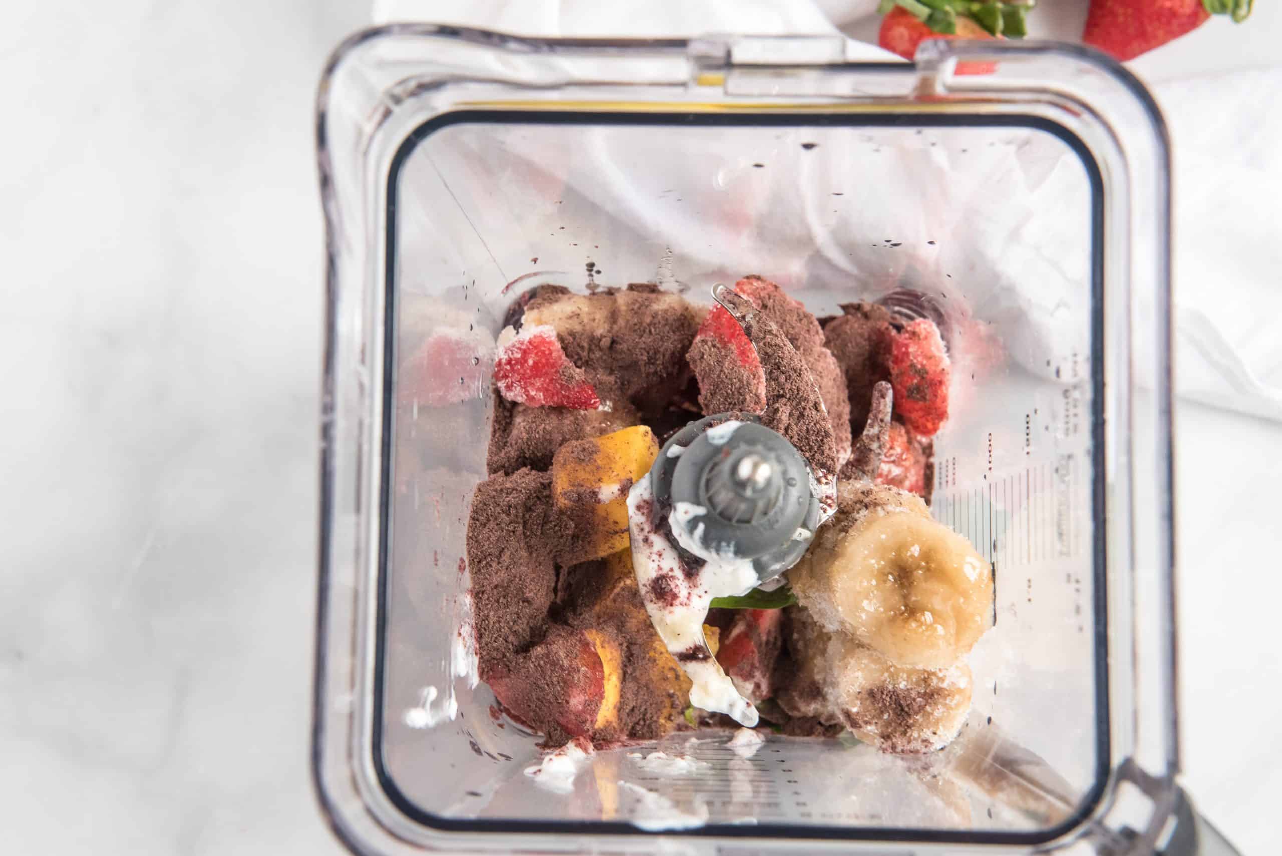 Smoothie ingredients in a blender on a white marble background.