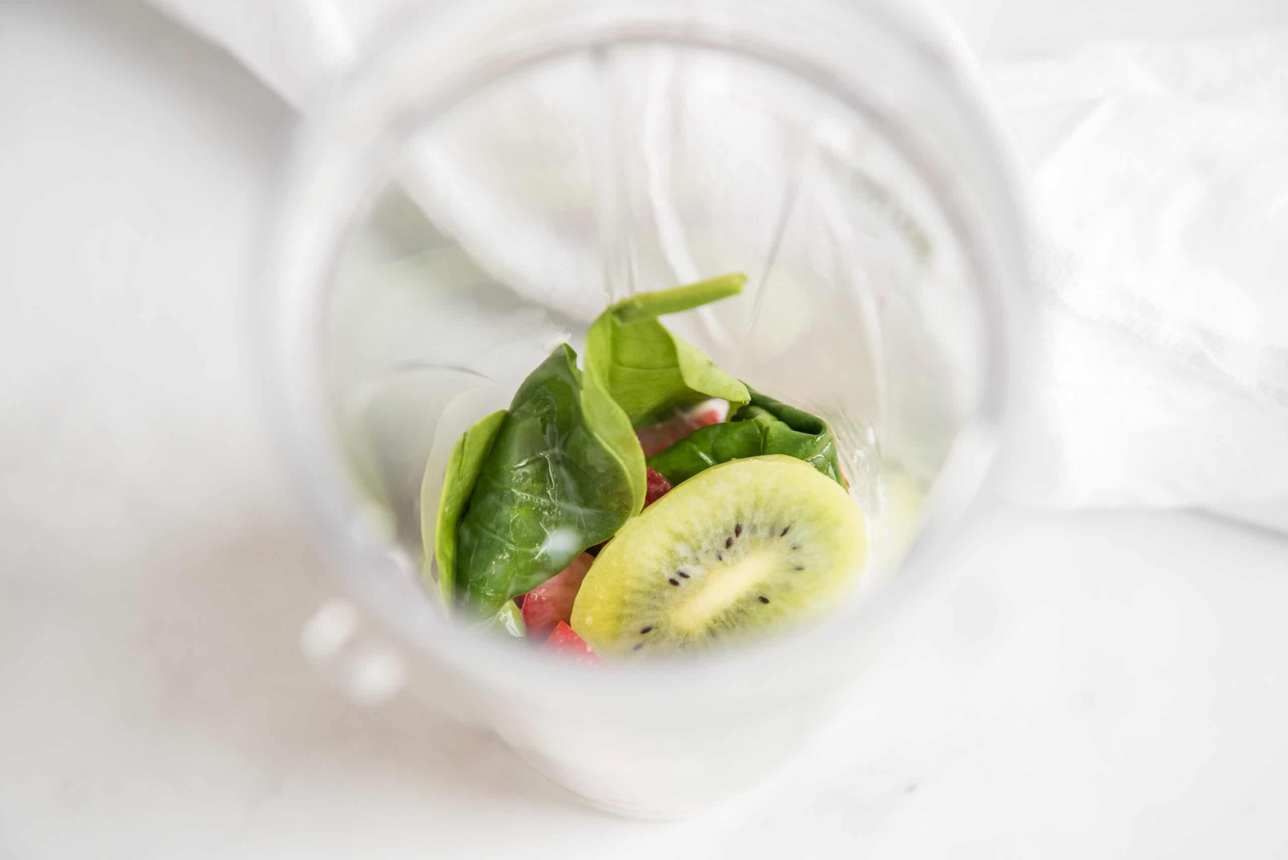 Kiwi fruit and baby spinach in a bullet blender on a white marble background.
