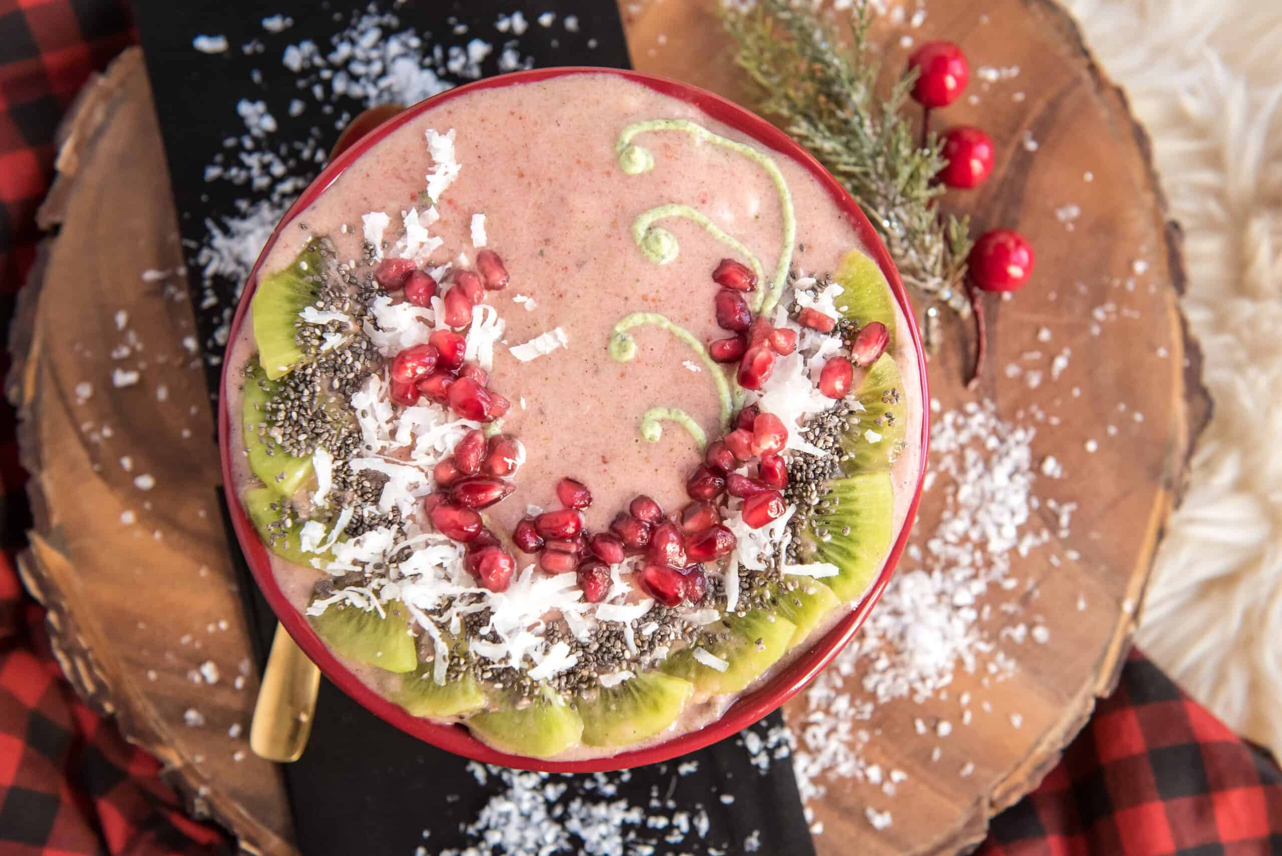 Holiday themed strawberry banana smoothie bowl on wood with a black napkin and red and black plaid table cloth.