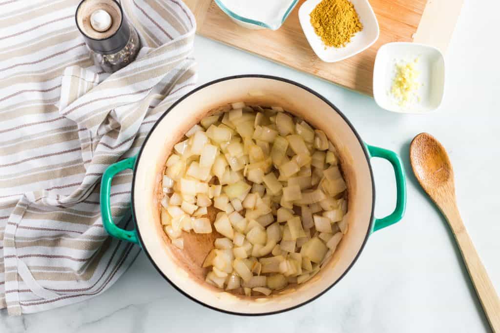 Diced onion in a large pot with spices and wooden spoon beside it.