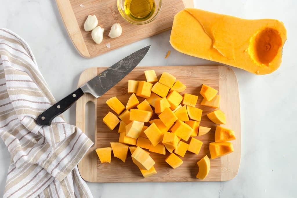 Butternut squash cut into chunks on a wood cutting board on a white background.