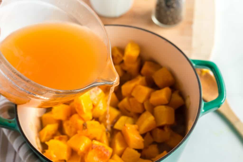Vegetable broth being poured into pot with butternut squash.
