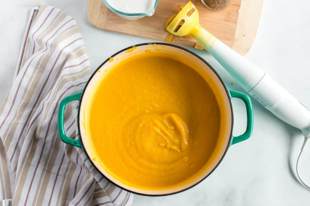 Butternut squash soup in bowl with immersion blender beside it.