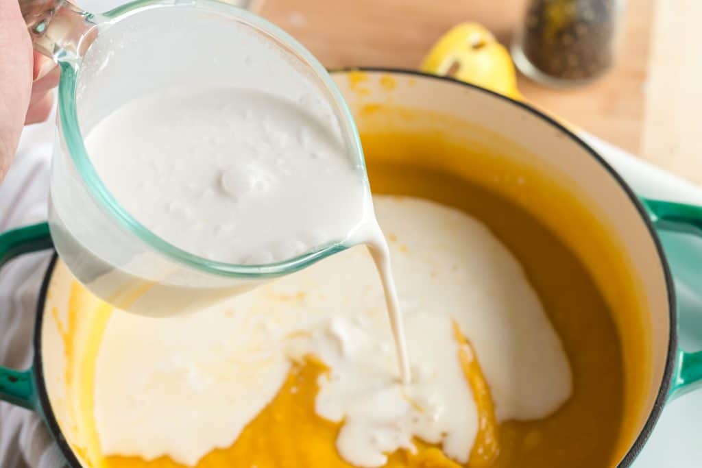 Coconut milk being poured into pot of butternut squash soup.