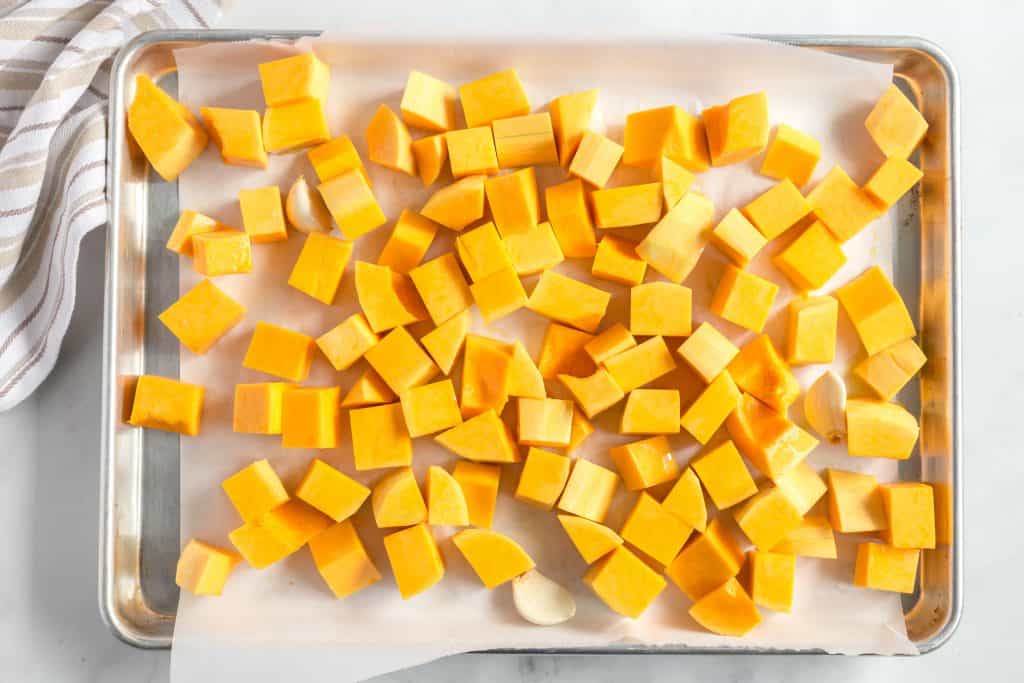 Butternut squash and garlic cloves on a baking pan.