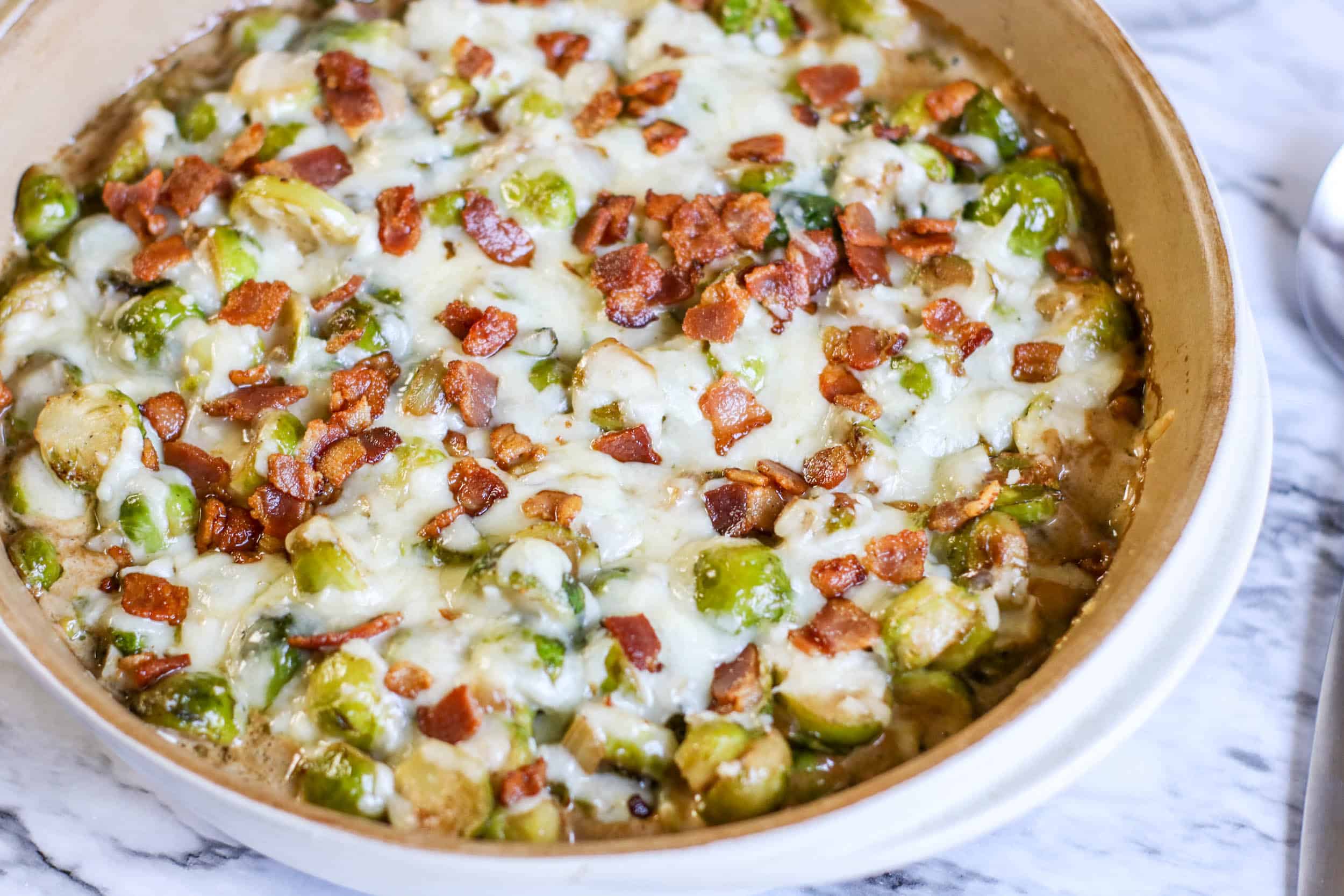 Cheesy Bacon Brussels Sprouts Casserole hot out of the oven on a white marble background.