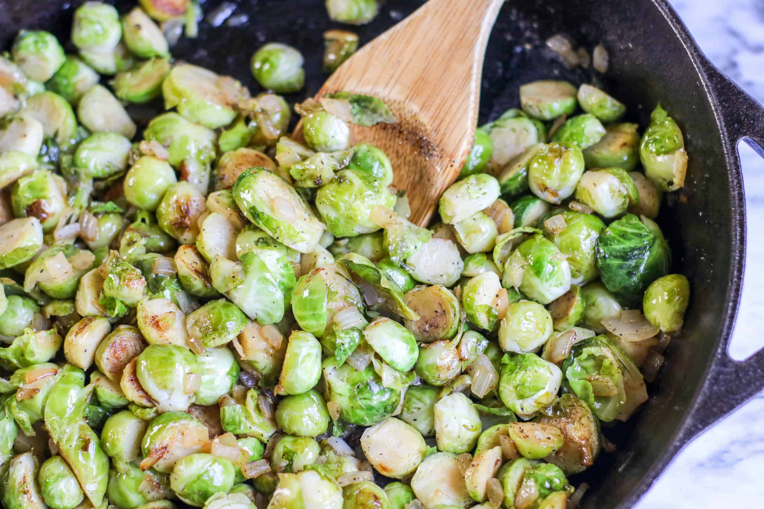 Brussels sprouts in a cast iron skillet with a wooden spoon.