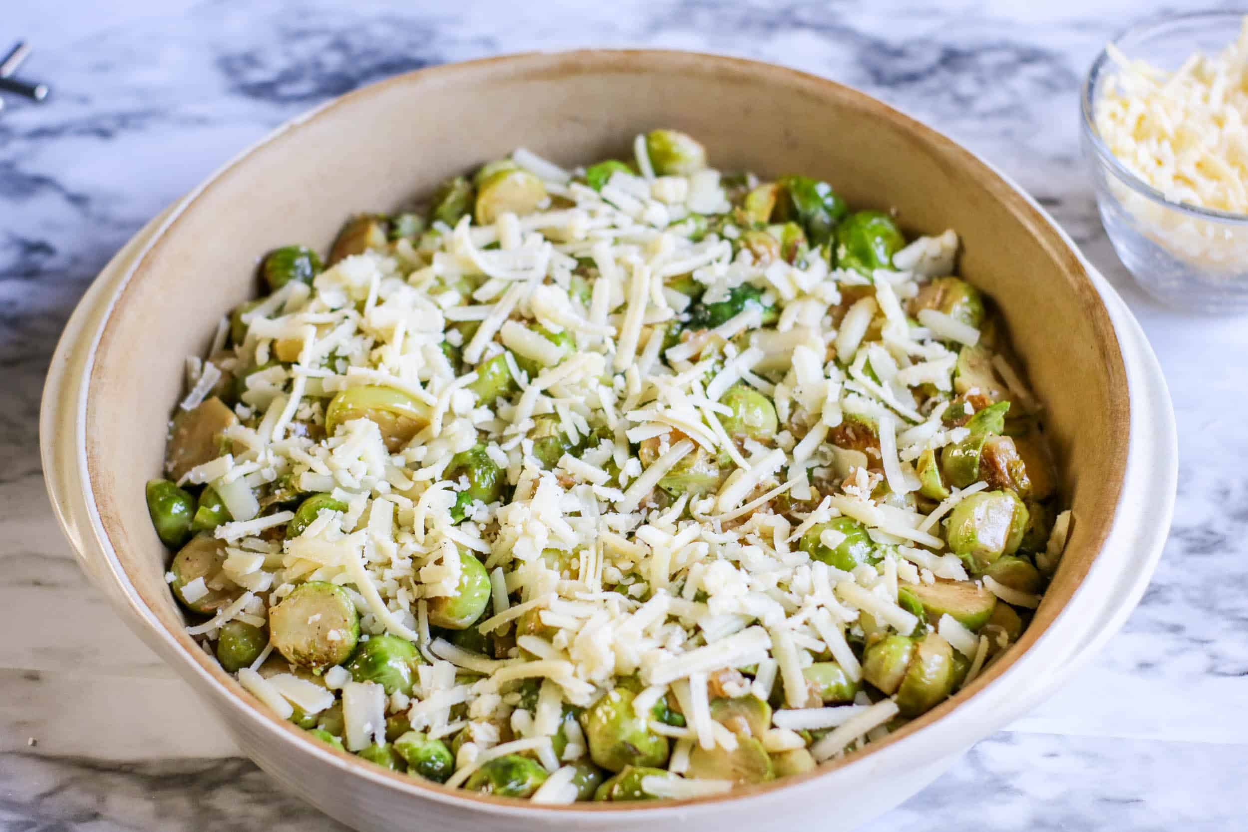 Brussels sprouts with cheese in a casserole dish on a white marble background.