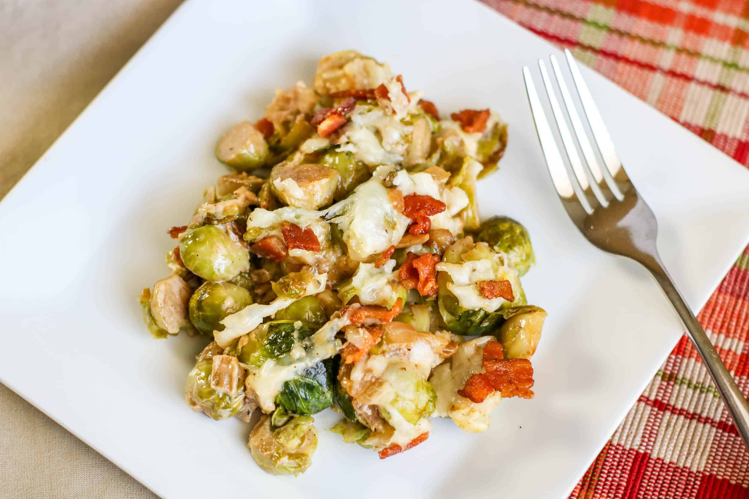 Cheesy Bacon Brussels Sprouts Casserole on a white plate with a fork and red plaid placemat.