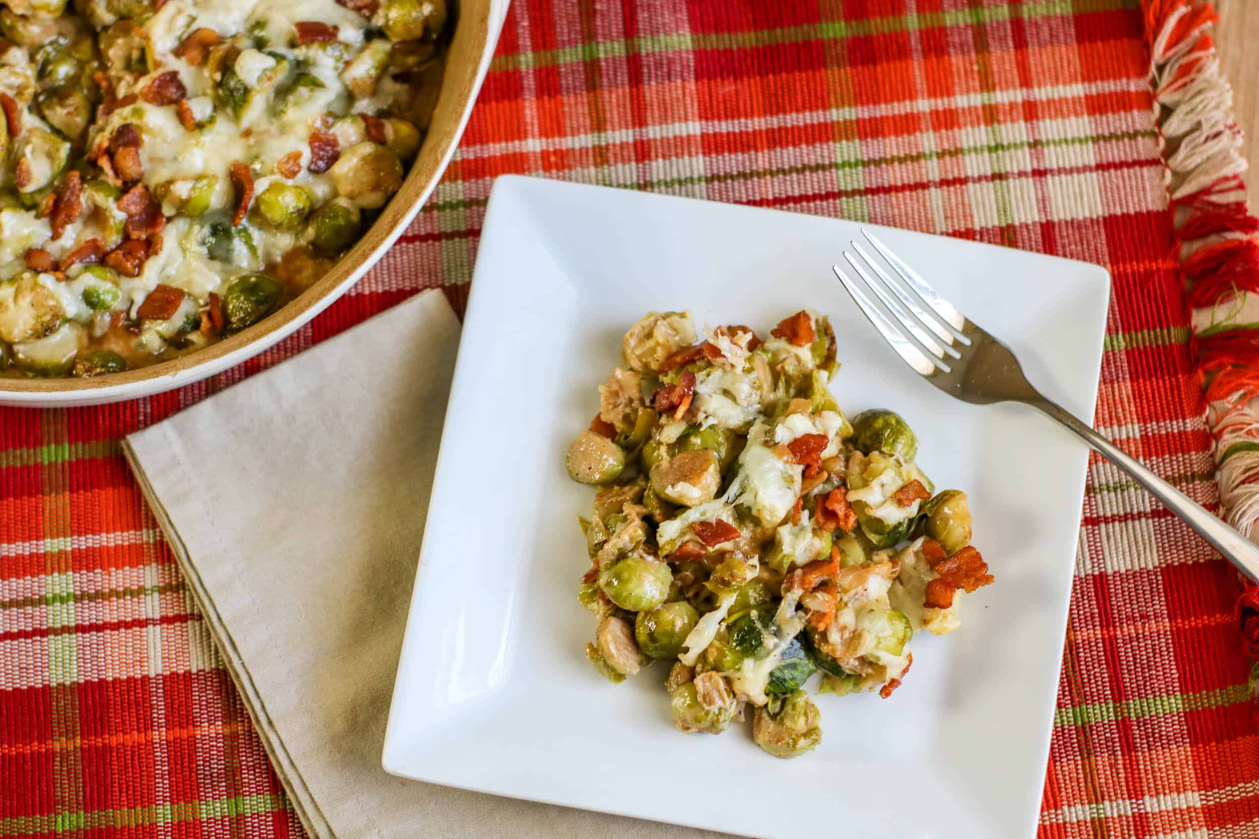 Cheesy Bacon Brussels Sprouts Casserole on a plate and in a casserole dish on a red plaid placemat with a napkin and fork.
