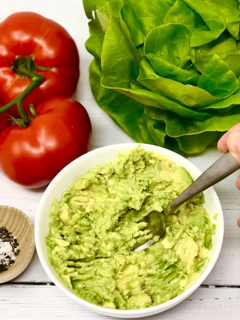 Mashing up avocado in a white bowl.