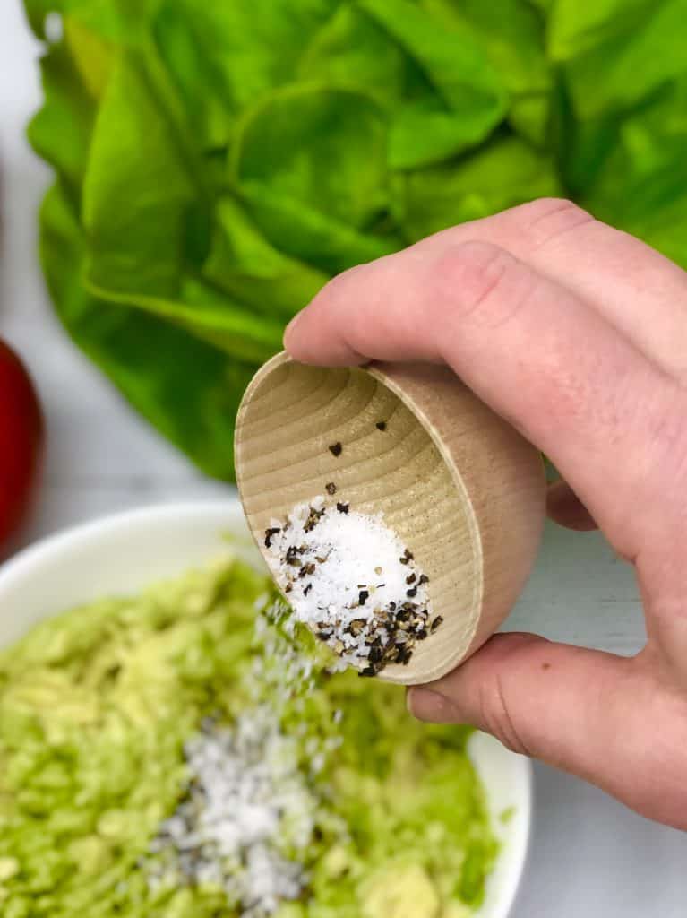 Adding salt and pepper to avocado.