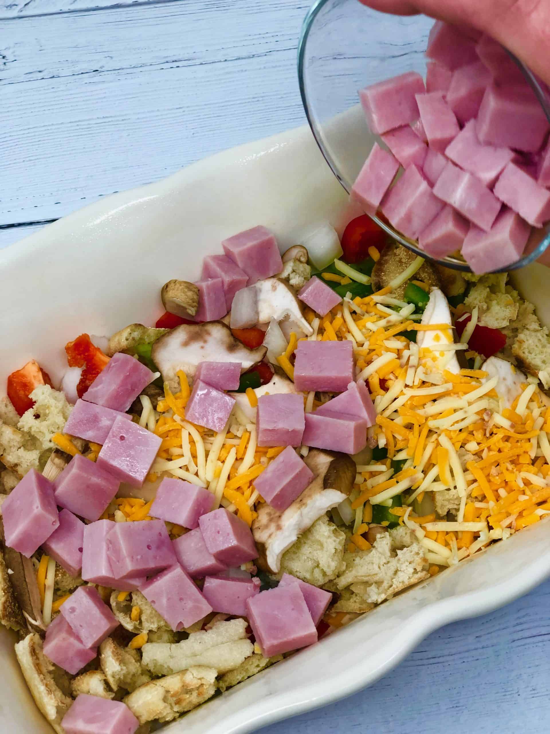 Diced ham being placed in a baking dish.