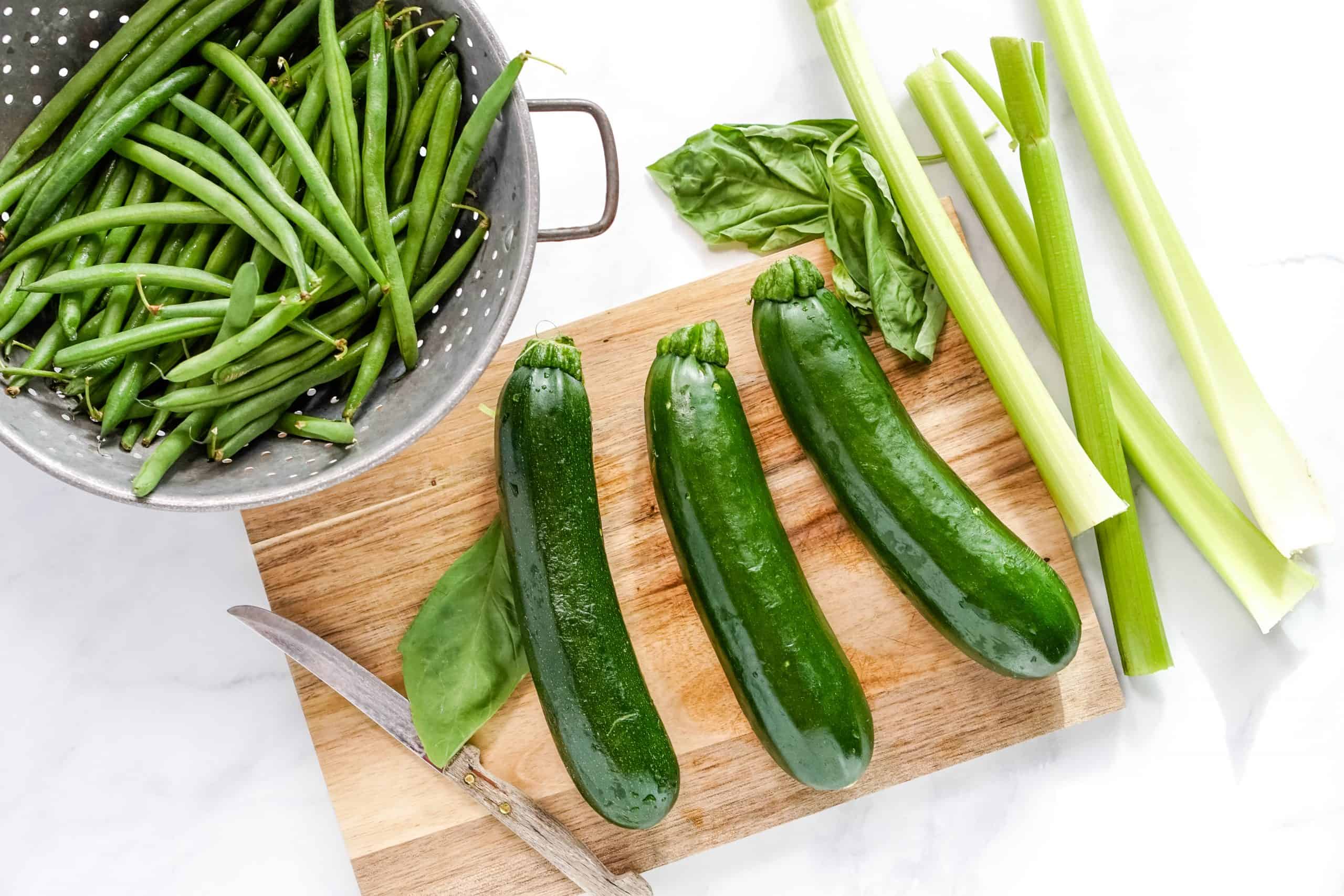 zucchini, celery, basil and green beans on a wood cutting board.