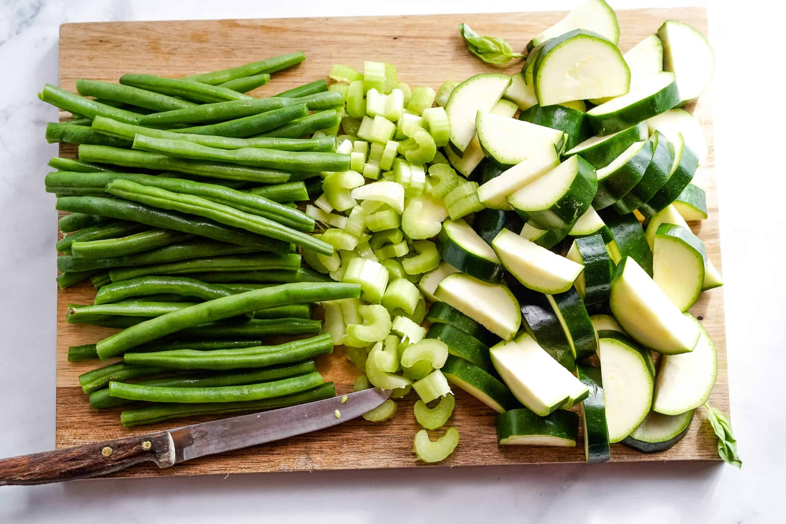 Green beans, chopped celery and zucchini on a cutting board.