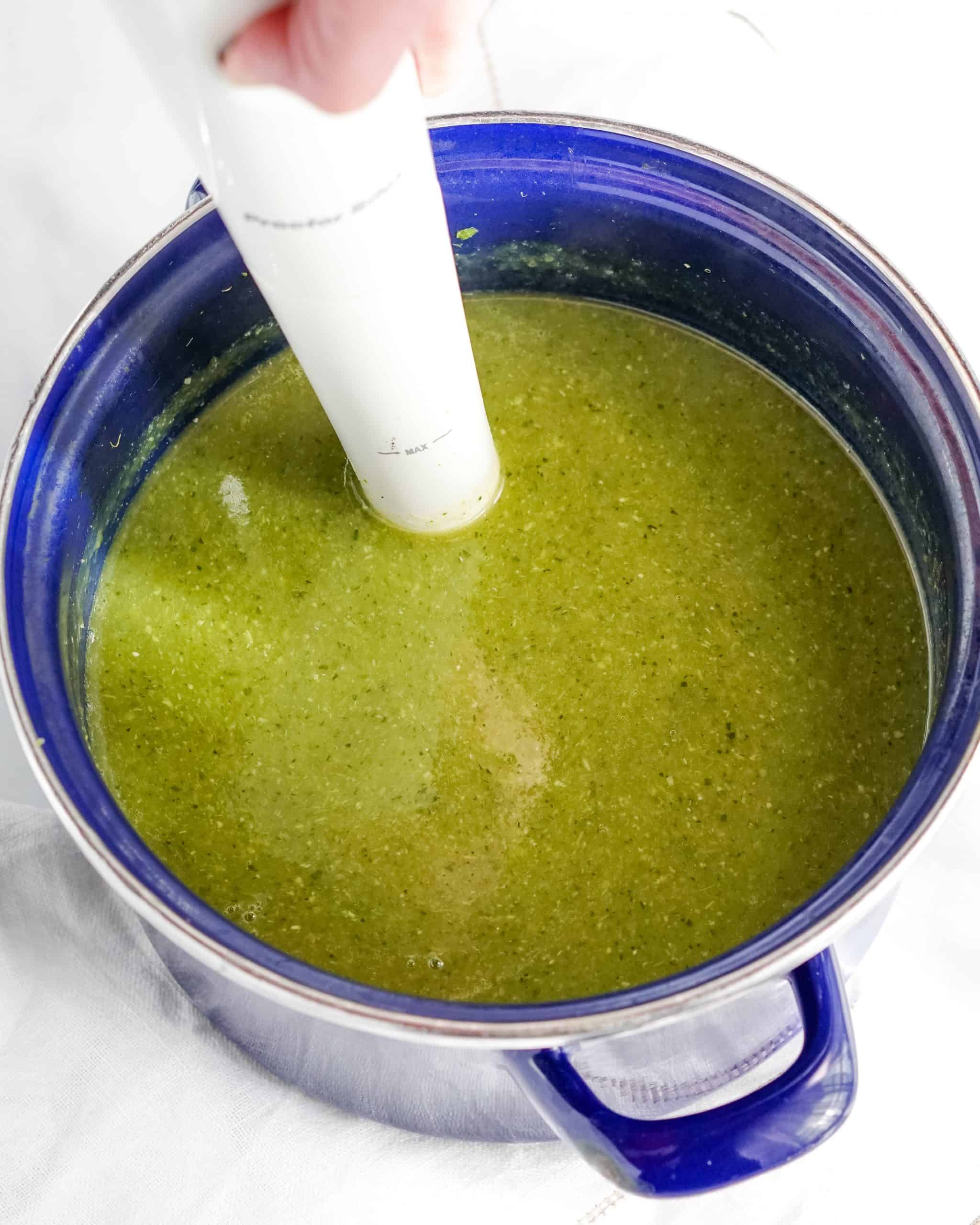 green broth and immersion blender in a blue pot.