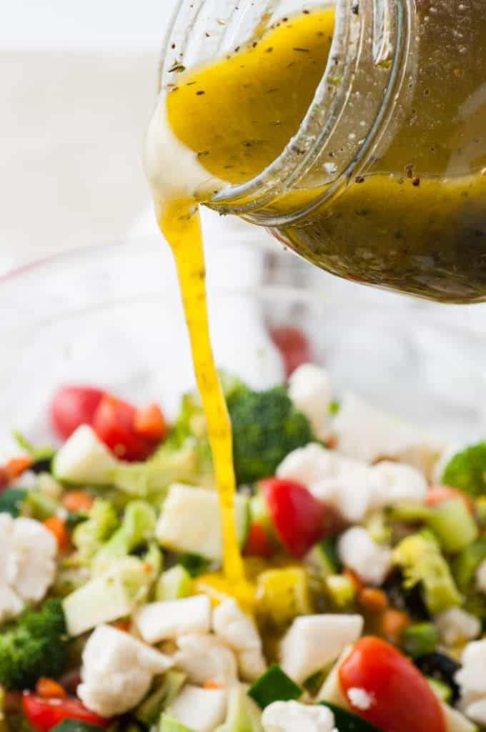 Italian dressing in glass jar being poured onto a salad.