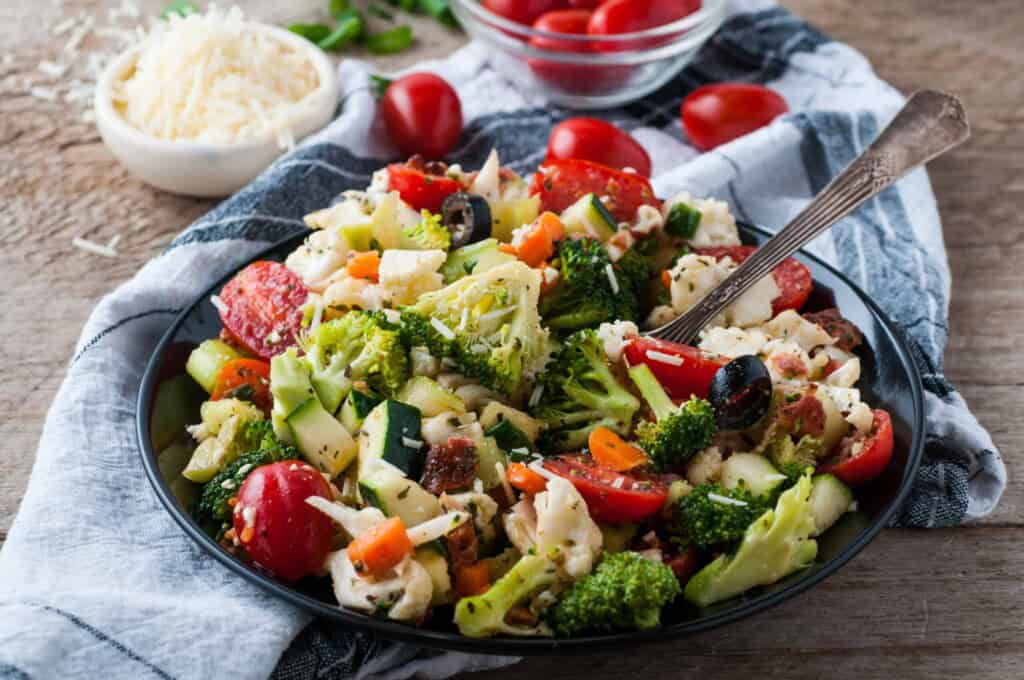 Crunch salad with fork in it on wood background with a bowl of Parmesan cheese and cherry tomatoes in the background.