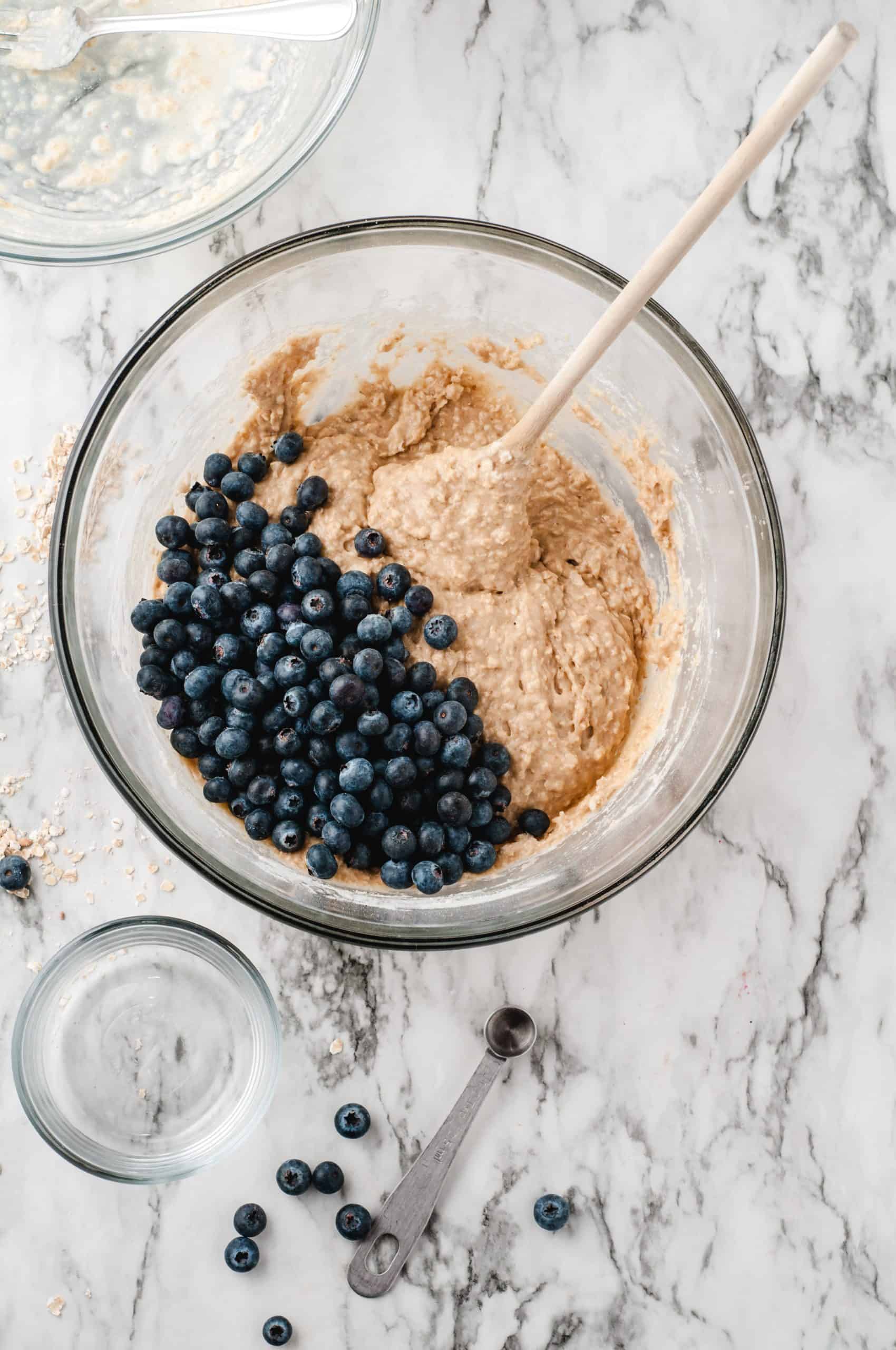 blueberries and muffin batter in a glass bowl.