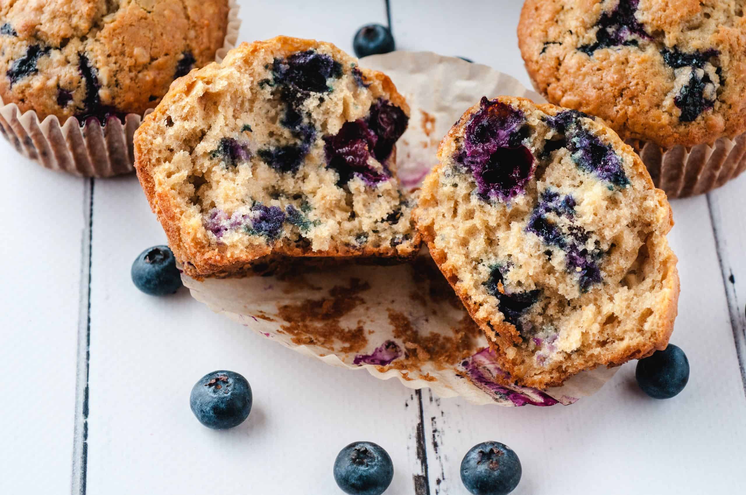 Fresh blueberry muffins with one broken in half on white background.