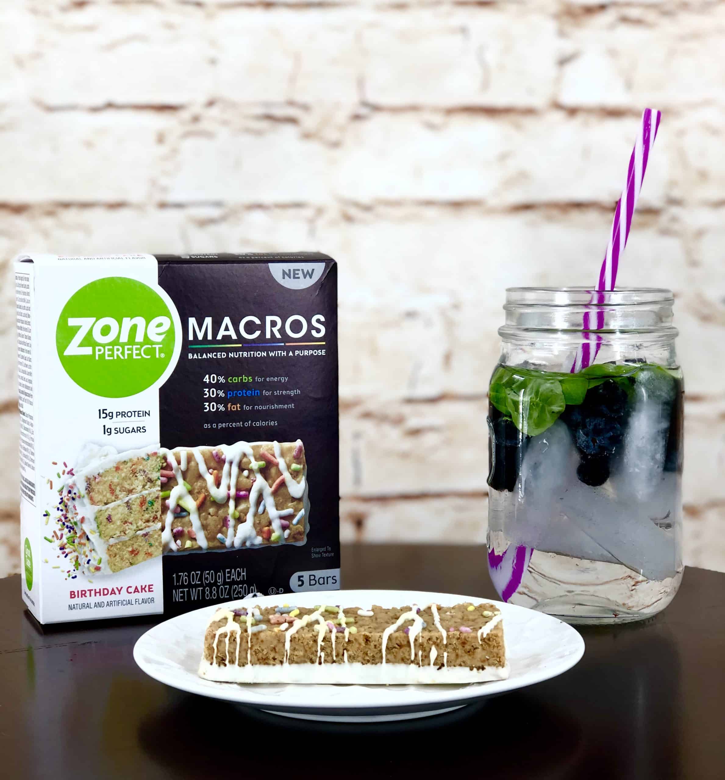 Water infused with berries and ZonePerfect Macro Bar on wood table with white brick background.