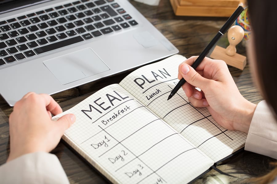Businesswoman Writing Down A Meal Plan In Checkered Notebook With Black Marker Over The Desk