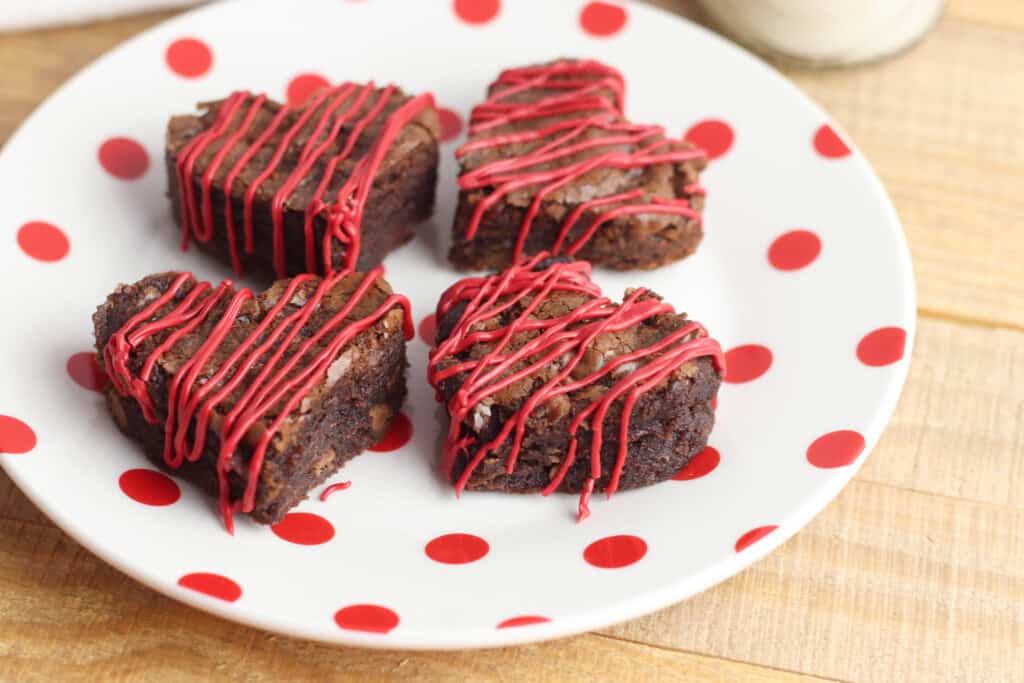 Heart-shaped brownies with red frosting drizzled on top on a white plate with red polka-dots.