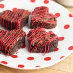Heart-shaped brownies with red frosting drizzled on top on a white plate with red polka-dots.